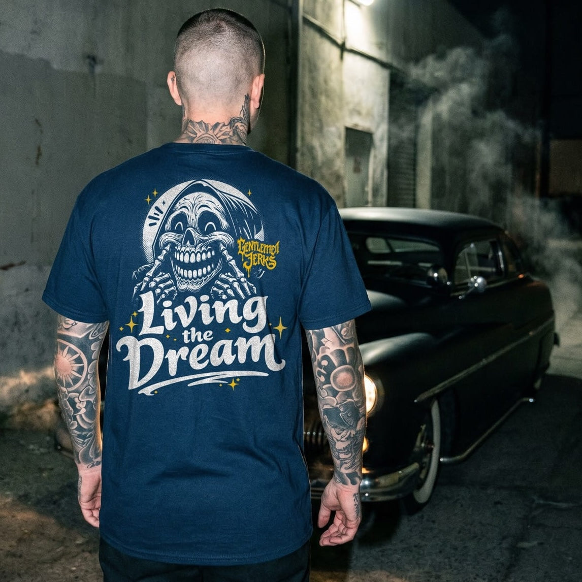 Man wearing a blue t-shirt with 'Living the Dream' graphic, standing in an urban setting at night.