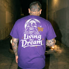 Person wearing a purple t-shirt with a graphic design and text, standing in a dark alley.