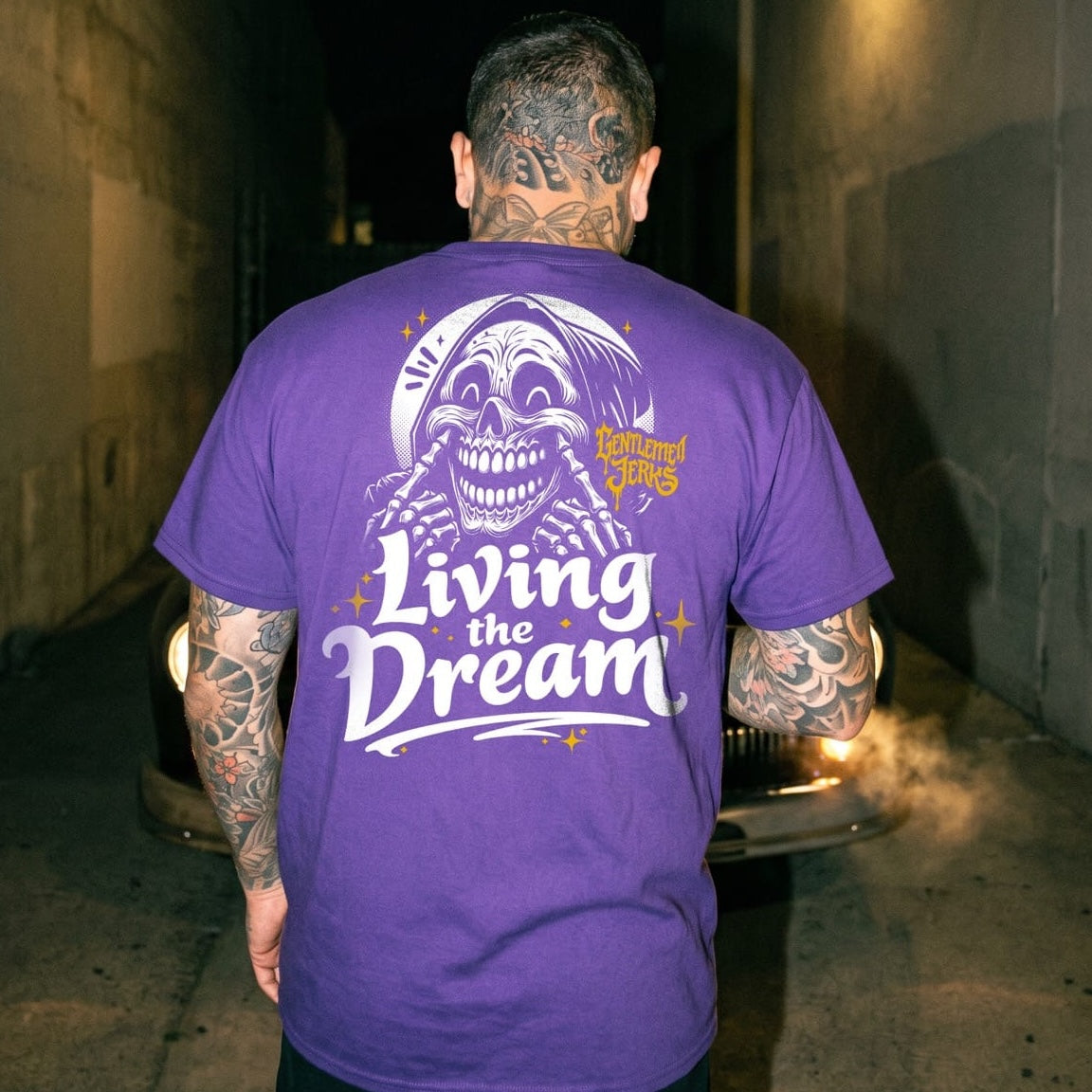 Person wearing a purple t-shirt with a graphic design and text, standing in a dark alley.