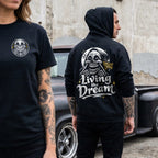 Two people wearing black t-shirts and hoodies with a skull design and text, standing in front of a vintage truck.