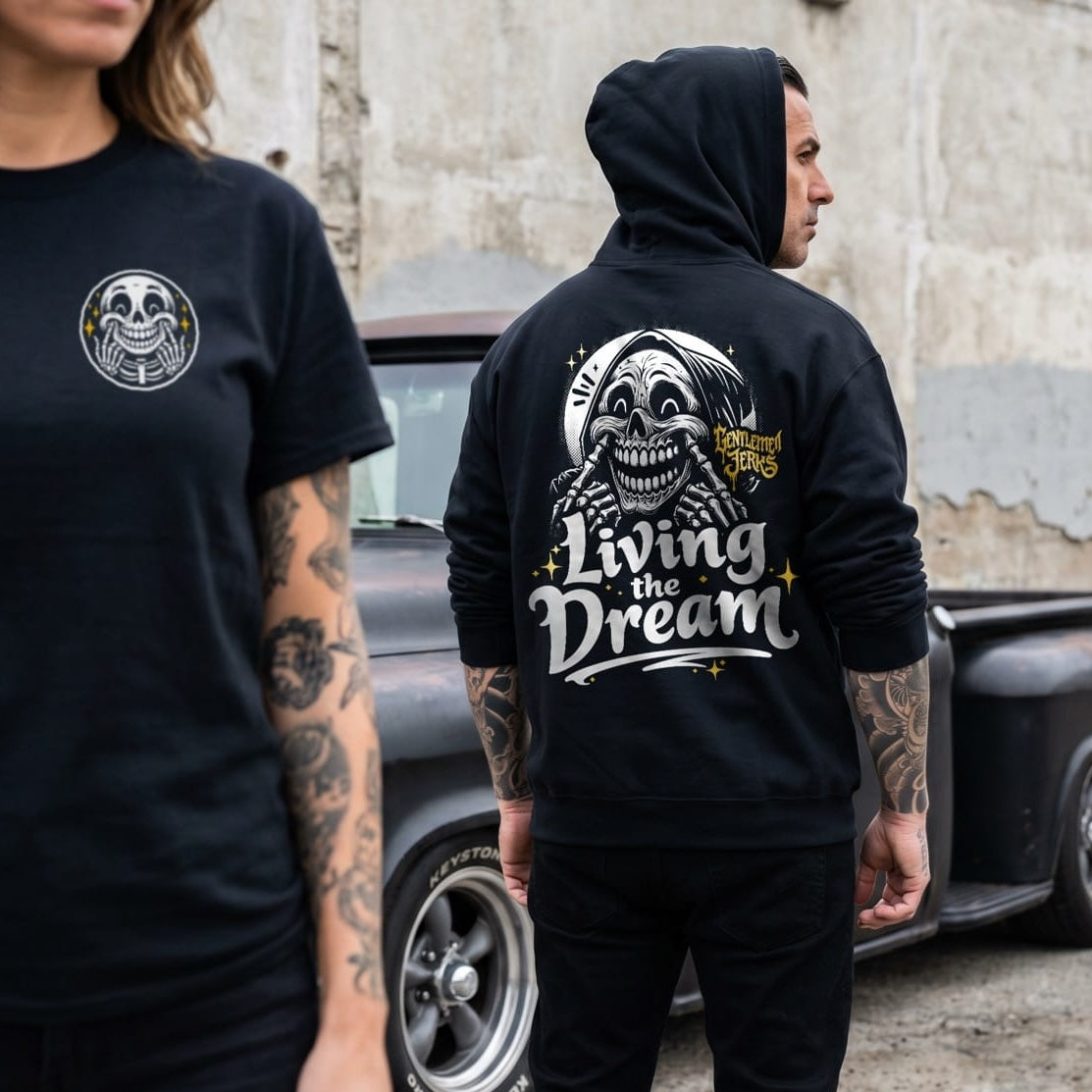 Two people wearing black t-shirts and hoodies with a skull design and text, standing in front of a vintage truck.