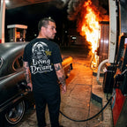 Man standing next to a burning car at a gas station at night.